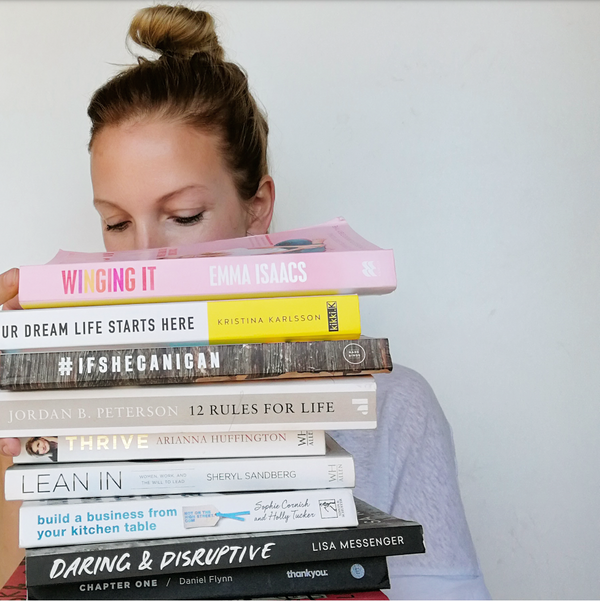 woman holding a stack of entrepreneur business books by leading start up and famous business owners  