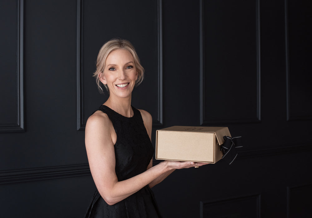 a lasy standing in a luxury suite holding a black bow gift hamper in Sydney
